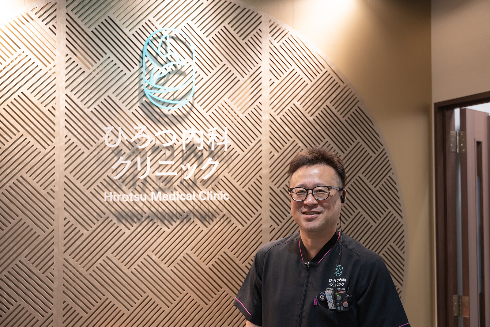 エントランスのロゴの横に院長が笑顔で立っている