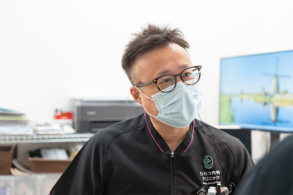 院長が診察デスクで説明している様子（電子カルテ端末も映る）